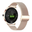 Back of rose gold NX23 Pro Smartwatch Mujer with Milanese band. Features glowing green heart rate/pedometer sensors, "WATER RESISTANT" text, CE/FC marks, and 5V-1A input on its black sensor panel. Studio shot.