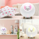 White spherical humidifier with a glowing pink/yellow smiling grey cat night light, on wood legs, emitting vapor. Set in a child's room. Real image.
