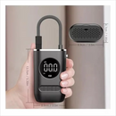 A compact, dark gray portable air pump, held by a hand. It features a digital display showing "00.0 PSI", a flexible gray hose, and bottom control buttons. Made of matte plastic, with overlaid dimensions. An oval top-view shows textured vents. Graphic design.