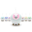 A line of seven spherical "Planet Cat" humidifiers with wooden legs. The front unit is light blue-white with a pink-lit smiling cat face, emitting vapor. Other units glow in blue, purple, orange, yellow, green.