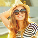 Smiling woman in black, oval Gafas Sol Bluetooth F07 sunglasses, straw hat, and striped shirt outdoors. Stylish frames with subtle side details, conveying audio tech. Warm, sunny real image.