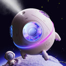 White spherical 'Spaceship Explorer' humidifier with glowing blue/purple LEDs, an astronaut figure inside, and mist output. It has pink accents & lands on a moon surface next to a mini astronaut. Graphic design.