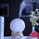 White textured moon aroma diffuser, showing lunar craters, on a light wood stand, emitting vapor. Stylish, realistic lamp for home decor. Real image.