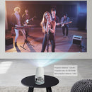 White cylindrical mini projector on a black table projects a vibrant rock band concert onto a wall. Specs overlay: Projection distance 1.2-4m, size 40-130 inches. Real product image with graphic text.