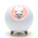 White spherical humidifier with a minimalist smiling white cat figure inside an orange-lit circular opening. It stands on three light brown feet and has a glowing orange exclamation mark below. Real product photo.