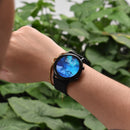 Smartwatch ZL73J on a wrist, featuring a round black case and textured silicone strap. The vibrant display shows 'WED 0301', '08:49', '0°' with a snowy mountain background. Real lifestyle image against green foliage.