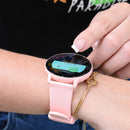 ZL02 Pro smartwatch on a wrist: round black screen displays 'Stress' and 'Measuring...' with Min/Max. Pink silicone band, glossy screen. A finger touches the display. Real photo, with a gold knot bracelet.