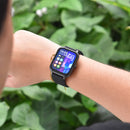 Real image: Person wearing a ZL54CJ smartwatch with a black rectangular display & silicone strap. Screen shows '10:03', 'MON 01-01', app icons, city skyline. Gold bracelet also worn. Outdoor green foliage background.