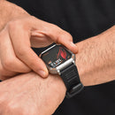 Man wearing a G106 smartwatch with a silver-grey angular case and black textured silicone strap. Its screen displays 10:12, MON 01, over a black background with a red leaf. Buttons are labeled "POWER" & "SPORT". Real photo.