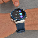 ZD5 Smartwatch on wrist. Silver case, blue bezel with compass markings & white numbers. Dark blue silicone strap. Round black screen displays NFC, assistant, health icons. Finger interacts with screen. Real image.