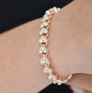Dainty rose gold-tone bracelet with interconnected heart links, each set with three sparkling, faceted clear crystals, worn on a wrist against a dark background. Real photo.