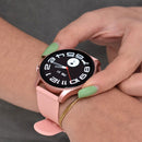 Rose gold Smartwatch KC88 with pink silicone strap on a wrist. Its round AMOLED screen shows a digital-analog clock with "FRI 31" and step counter. A hand with green nails adjusts the display.