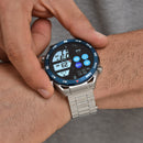 Man's hand adjusts a silver-tone ZD5 smartwatch with a blue rotating bezel and metal link band. The black touchscreen displays time, date, heart rate, & app icons. Nautical-style numbers mark the bezel. Real image.