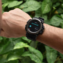 Black rugged Smartwatch LC16 on a man's wrist, displaying "Walking 00:03:45, 14 Steps" on its round color screen. Features a black rubber strap, dark grey metal bezel with "SPORT WATCH" and "WATER RESIST". Real photo, blurred green background.