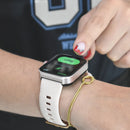 A person's hand taps a Smartwatch NX22 with a silver bezel and black screen showing "Start" and "GPS" in Spanish. It has a white silicone strap with holes, worn on the wrist, alongside a gold-colored bracelet. Real photo.