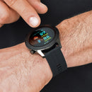 A hand taps a black SmartWatch F22U on a wrist. Its round display shows 89 prbpm, 98 SpO2%, and 09:49. The watch has a dark metal case, black silicone strap, and "SMART WATCH" text on the bezel. Real photo.