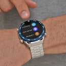 ZD5 smartwatch on a man's wrist. Silver stainless steel case, metal link band, blue bezel with compass marks. The round black screen displays "Asistente", "no en sang!" (oxygen), and "n arterial" (pressure) icons. A finger touches the display. Real photo.