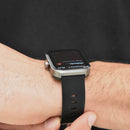 A real photo of a Smartwatch NX22 with a silver metal case and a black silicone strap worn on a wrist. Its rectangular AMOLED screen shows heart rate data like "Midiendo..." and time "08:42".