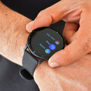Person's hand interacts with a black round SmartWatch ZL02 Pro on their wrist. The matte silicone strap and screen showing 'Heart Rate,' 'Sleep,' and 'Activity' with colorful icons are visible. Real image.
