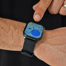 Real image: A hand taps a black square smartwatch with a textured silicone band. Its colorful screen displays 17:04, 15/03, and 83 steps, showing a modern design.