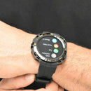 Rugged Smartwatch NX18 with a dark metallic gray case and black rubber strap on a wrist. Its round display shows 'Daily Activities,' 'Call,' 'Heart Rate,' 'Blood O' and the bezel features compass points. Real photo.
