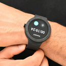 Smartwatch NX18 with a matte black silicone strap on a wrist, displaying a stopwatch showing 00:19:24 and a pause icon. Features a round dark screen and a numbered bezel. Real image.