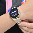 NX23 Pro smartwatch on a woman's wrist. Features a gold-toned case, faceted bezel, round screen with a purple cat face & "16:49", and a light beige silicone strap. Real image for health & calls.