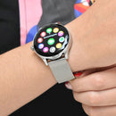 NX23 Pro Smartwatch on a woman's wrist, featuring a round silver-tone metal case and a textured Milanese mesh band. The vibrant display shows colorful app icons and "Notificaciones". Real photo.