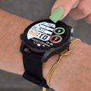 Black smartwatch with round AMOLED display showing 01:24 time, health stats (BPM), and date, worn on a wrist with a black silicone band. A finger with green nail polish touches the screen. A gold bracelet is also visible. Real image.