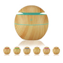 Wood-grain aroma diffuser with teal LED light accent & power symbol. Includes smaller diffusers showcasing red, green, blue, yellow, purple, orange light options. Modern design, graphic render on white.