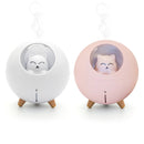 White & pink Planet Cat humidifiers/diffusers. Spherical plastic bodies, each with a clear dome showcasing a cute cat night light. Mist rises from the top. Stands on wooden legs. Real image.
