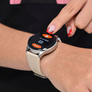 NX23 Pro Smartwatch Mujer on a wrist, featuring a round silver case and nude silicone band. A finger taps its black screen showing "Este Día", "2000/01 Lun", and "03". Real photo.