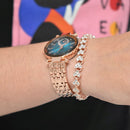 Reloj Reginald P719 rose gold watch on wrist, featuring a blue diamond-cut crystal dial & link band. Accompanied by a sparkling heart-shaped diamante bracelet. Real image.