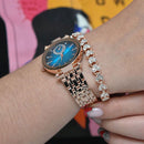 Reginald P719 rose gold-tone watch with a blue dial, diamond-cut crystal, and crystal hour markers, worn on a wrist. Adjacent is a matching rose gold bracelet with heart-shaped crystals. A real product photo.