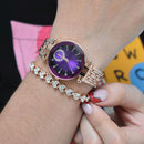 A woman's wrist displays a rose gold Reginald P719 watch with a purple dial under diamond-cut crystal, crystal markers, & an embellished sub-dial. Below it, a matching rose gold pavé crystal heart-link bracelet. Real photo.