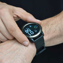 Man adjusting a SmartWatch NX9 with a dark gray textured bezel and black silicone strap on his wrist. The Amoled screen shows digital time (01:58), date, and fitness icons. "UP" is visible on a button. Real photo.