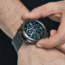 NX1 Pro smartwatch on a man's wrist. Dark gray metallic case and link band, black digital display shows time, date (WED 01:54), 40% battery, and fitness data. Elegant round design with red bezel accents. Real photo.