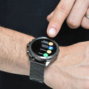 A finger interacts with the elegant dark metallic NX1 Pro smartwatch, featuring a round screen and metal link band. The display shows 'Llamar,' 'Contactos,' & 'Registro de llamadas,' highlighting its Bluetooth call functionality.