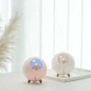 Two spherical "Planet Cat" humidifiers, one pink with blue light and one white with pink light, each featuring a cat figure inside a clear dome, wooden feet, and an exclamation mark button. Real image.