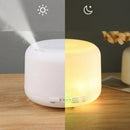 White V-M500 ultrasonic humidifier on wood, split image. Left: mist output shown with sun icon. Right: warm yellow LED light glowing with moon icon. Controls for Light, Mist, High/Low, and timer (60-180 min) are visible. Modern design.