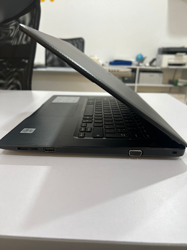 Black DELL VOSTRO 3490 laptop, partially open, showing its textured black surface. A side view highlights USB, SD card, and VGA ports, with an Intel sticker visible. Real photo on a white desk.