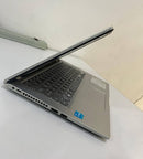 Used silver ASUS VivoBook X415EA laptop, partially open on a white surface. Shows black keyboard, touchpad, side ports, and an Intel Core sticker on the palm rest. Real product photo.