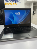 Used DELL Inspiron 3493 laptop with silver-white base, black keyboard & dark carbon fiber pattern palm rest, showing DELL stickers. Screen on, displaying blue abstract wallpaper, "03:57", and DELL logo. Real photo.
