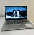 Open silver ASUS VivoBook X415EA laptop on a white desk. It has a black screen bezel, dark grey keyboard, and touchpad. Screen displays two penguins. Intel Core & ASUS X415 branding visible on the palm rest. Real image.